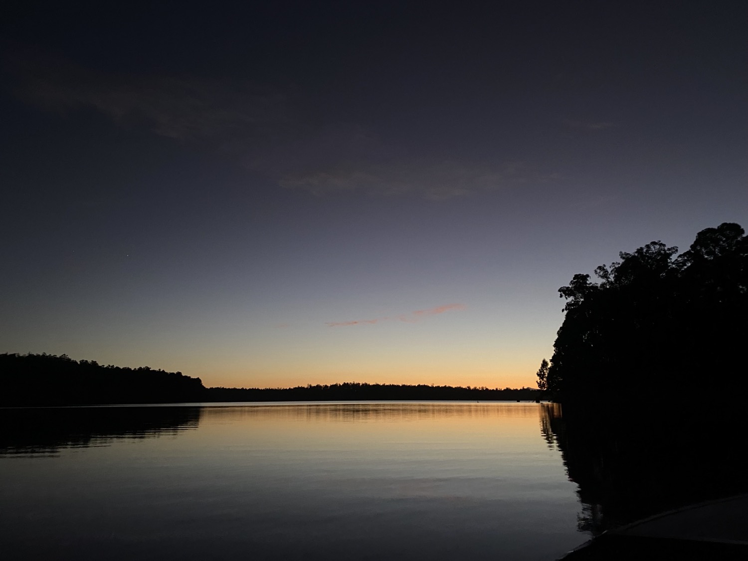 A still lake at dusk, hills dark against the last light