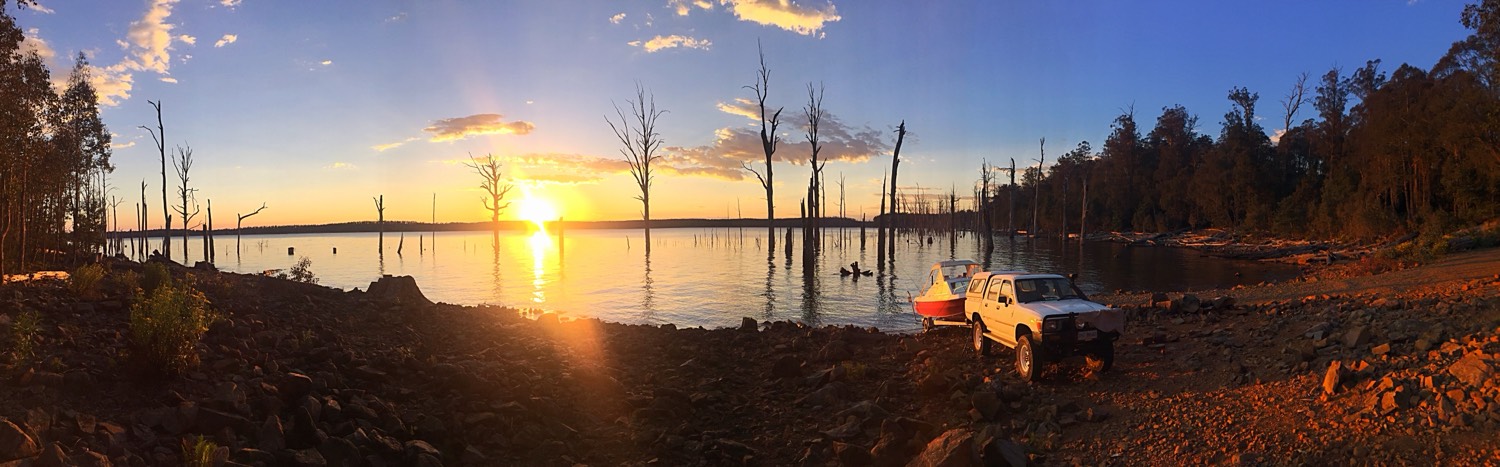 Sunrise over a Tasmanian lake, with a boat and a ute on the shore